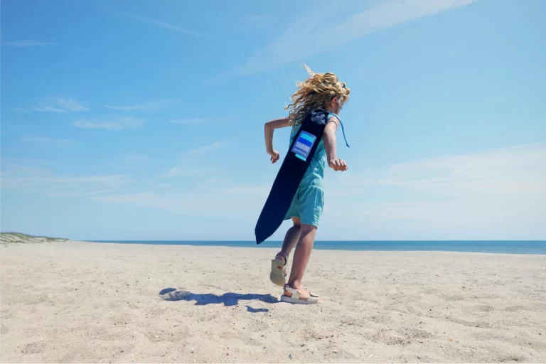 little girl running on sand at the beach with shibumi shade on shoulder